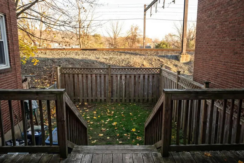 Narrow back yard of a brick twin enclosed by a 6 ft cedar board fence with an open lattice topper, rail line beyond