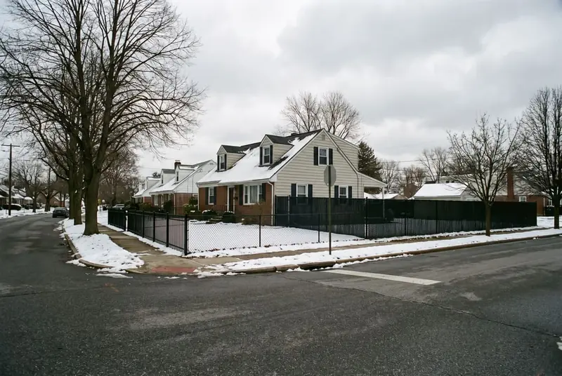 Black vinyl-coated chain link fence around the back yard of a 1950s Cape Cod on a corner lot in winter