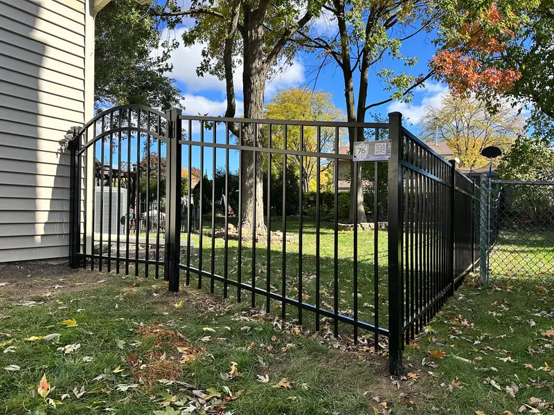 Black aluminum fence with an arched walk gate at the corner of a house