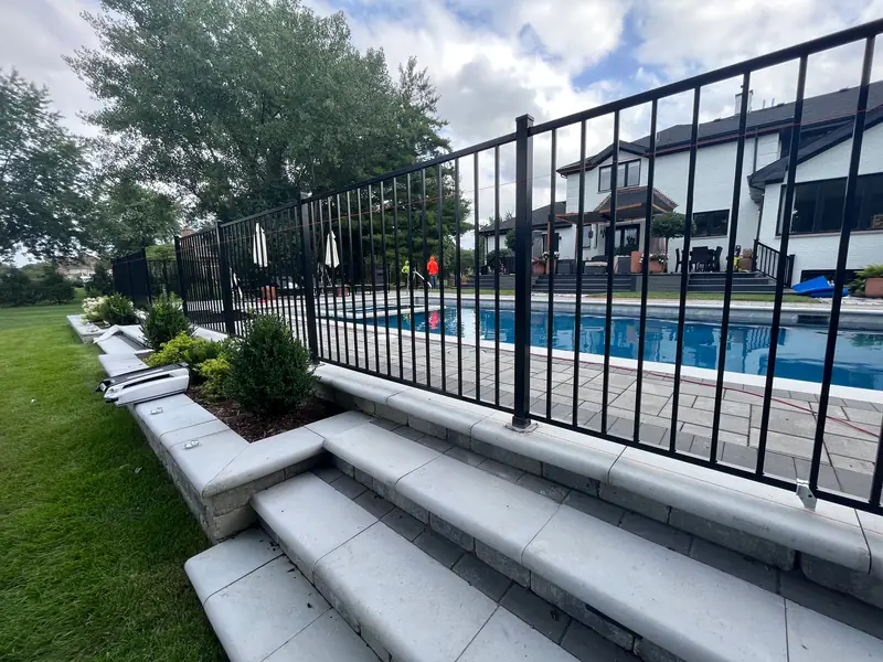 Black aluminum pool fence along a paver pool deck and stone steps