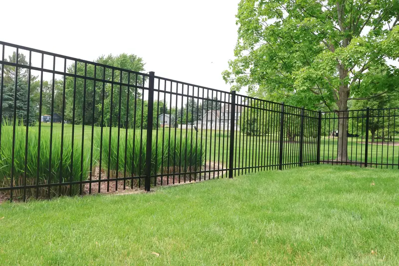 Black aluminum fence behind ornamental grasses at the edge of a lawn
