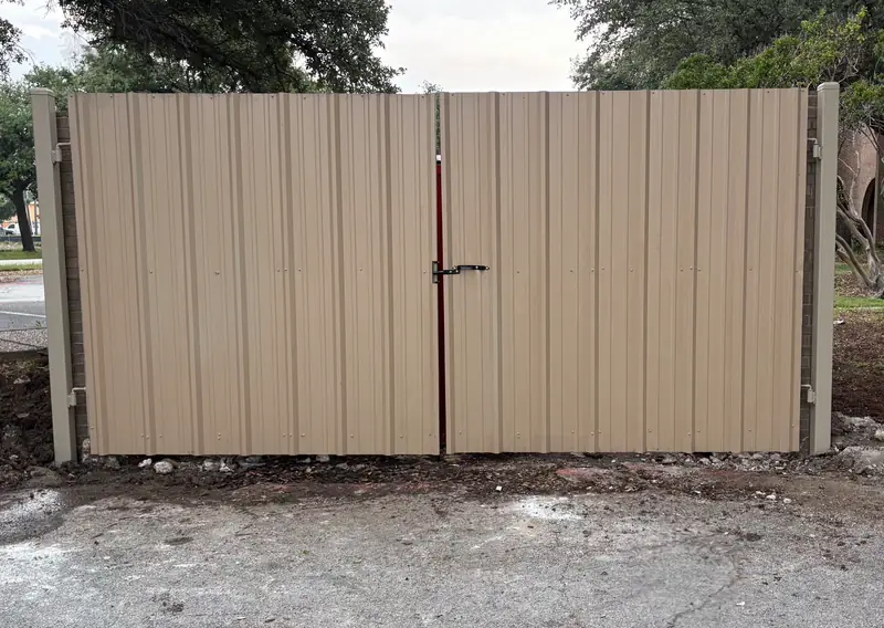 Tan ribbed metal-panel dumpster enclosure with double swing gates