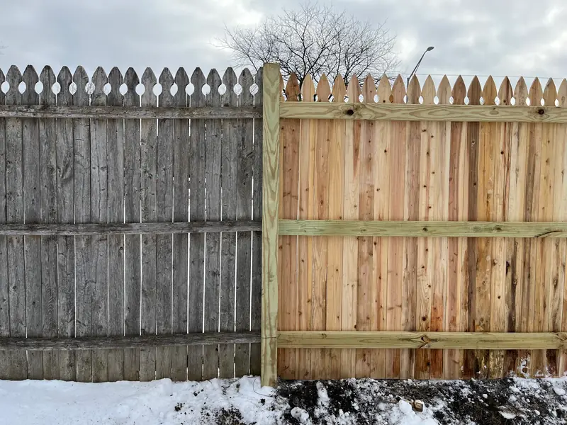 New wood fence section with pointed French Gothic tops installed beside an old, weathered section